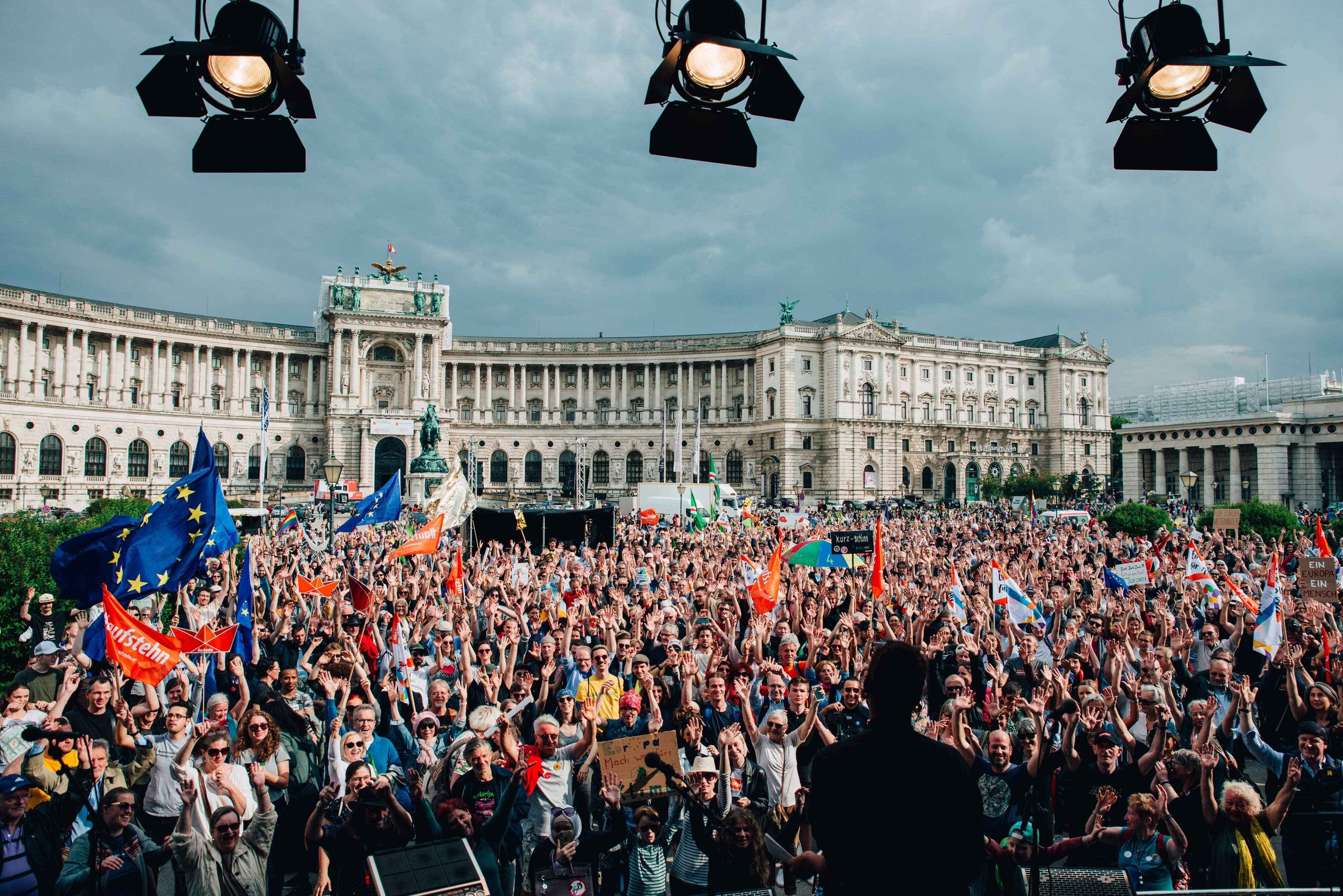 Zdjęcie przedstawiające tłum ludzi zgromadzonych na placu miejskim, trzymających flagi EU i inne