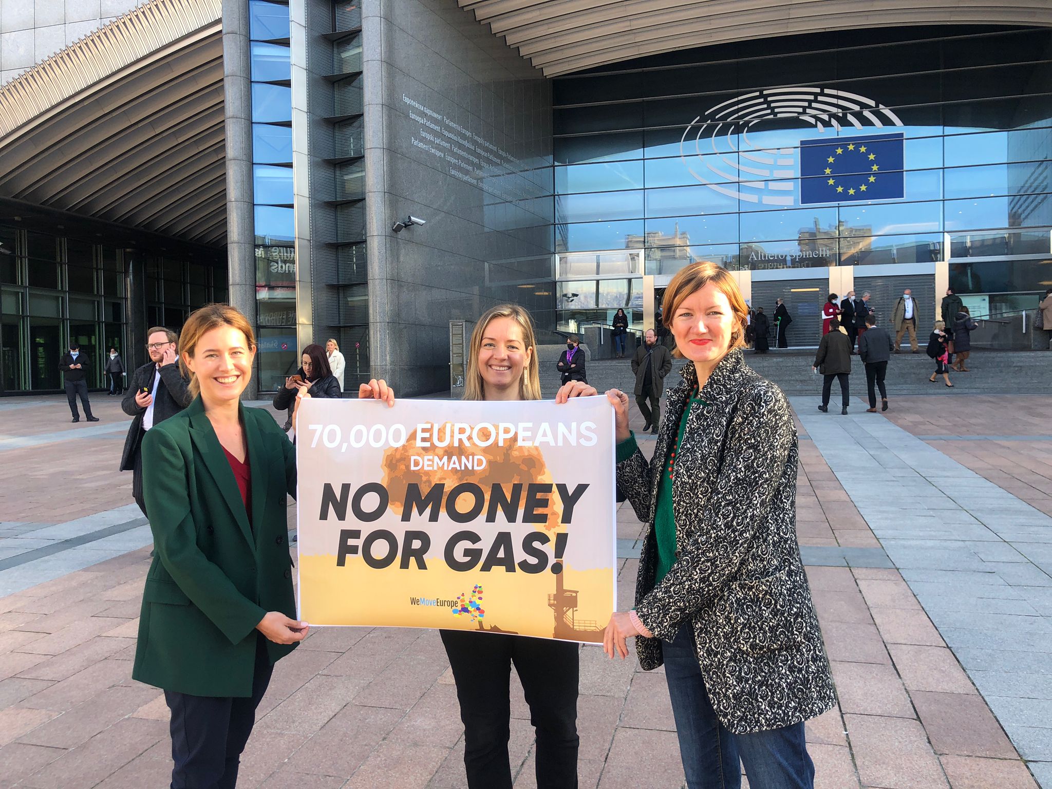 Zdjęcie przedstawiające trzy osoby trzymające baner z napisem 'Koniec finansowania gazu', stojące przed budynkiem unijnej instytucji